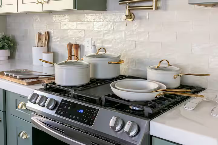 Bright chef's kitchen with gas range, sage cabinets, and quality cookware
